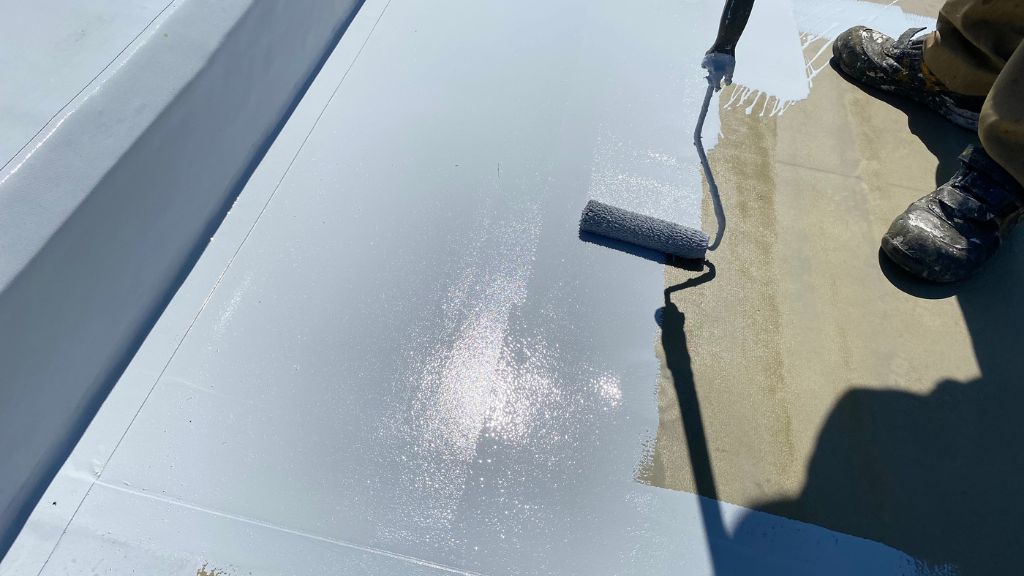 屋上の防水工事でローラで塗料塗布中