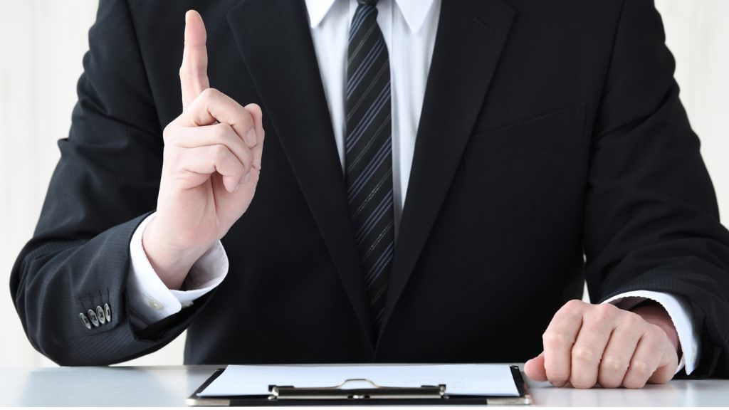 スーツを着た男性の胸元、右手で人差し指を立てている