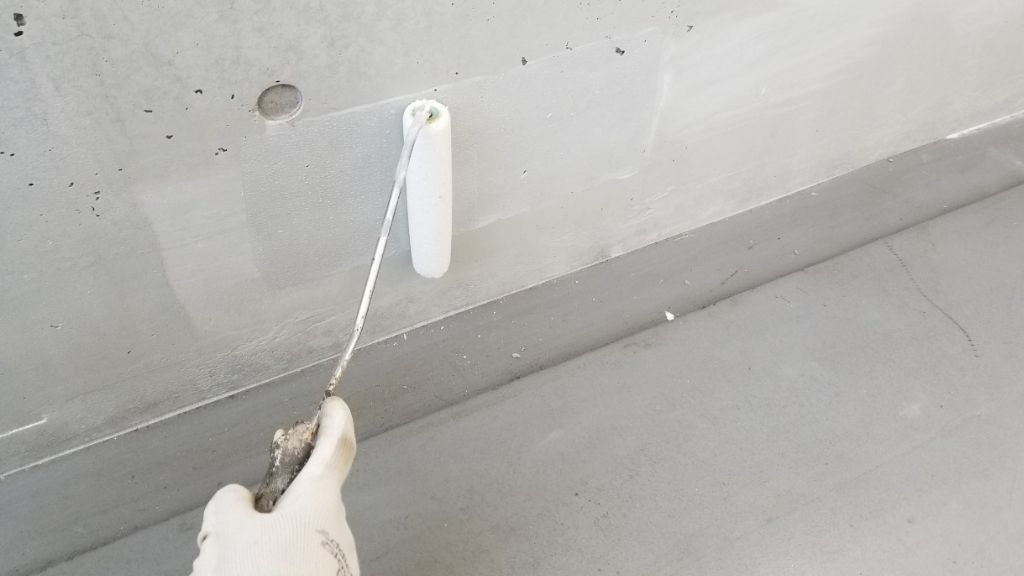 コンクリート壁をローラーで塗装している